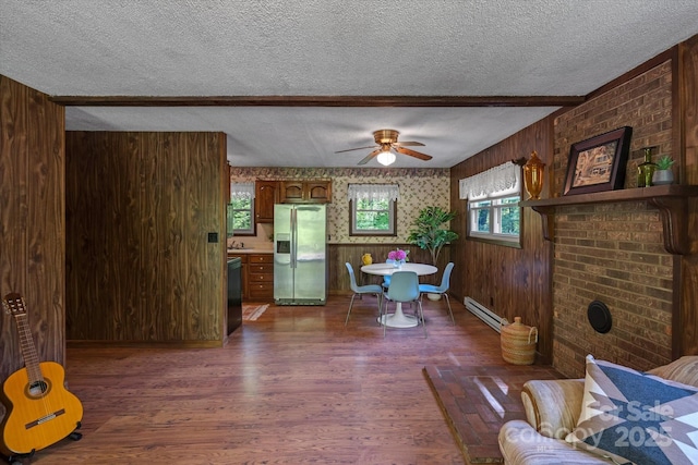 living room with baseboard heating, a textured ceiling, a ceiling fan, dark wood-type flooring, and wooden walls