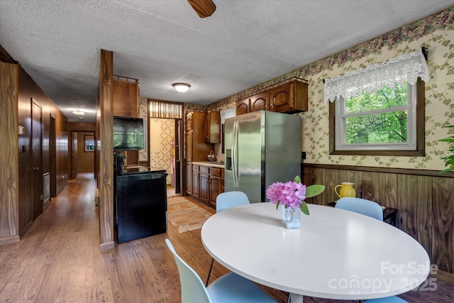 kitchen with wallpapered walls, stainless steel fridge with ice dispenser, wainscoting, light wood-style floors, and a textured ceiling