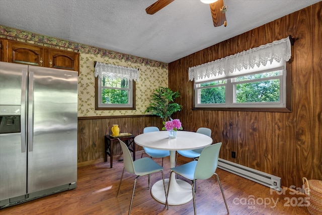 dining space featuring a baseboard heating unit, a ceiling fan, wood finished floors, a textured ceiling, and baseboards