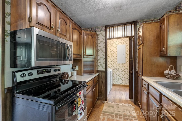 kitchen with appliances with stainless steel finishes, wallpapered walls, light wood-style floors, brown cabinetry, and light countertops