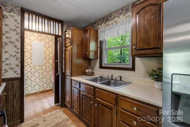 kitchen with wallpapered walls, stainless steel refrigerator with ice dispenser, a sink, light wood-style flooring, and light countertops