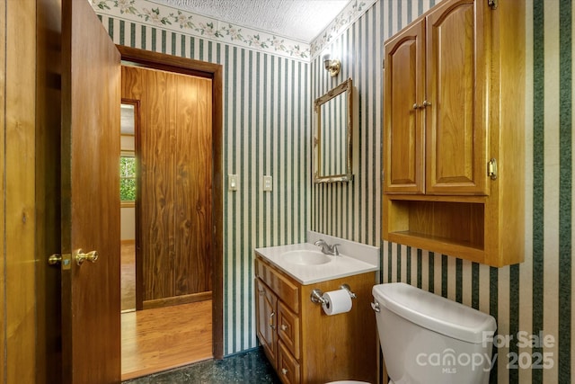 half bathroom with wallpapered walls, toilet, and vanity