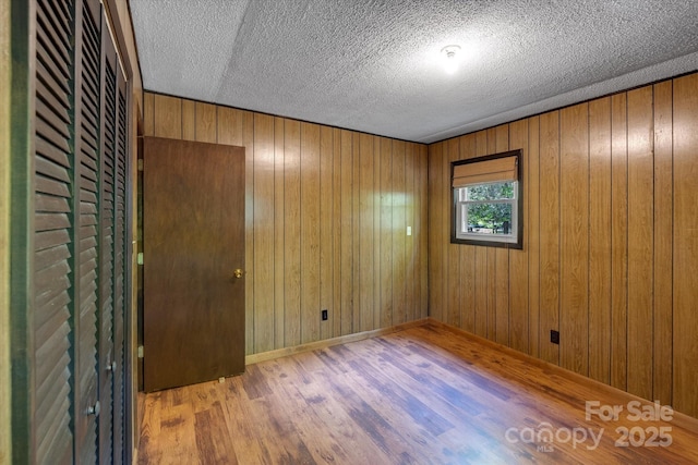 spare room featuring wood finished floors, a textured ceiling, wood walls, and baseboards