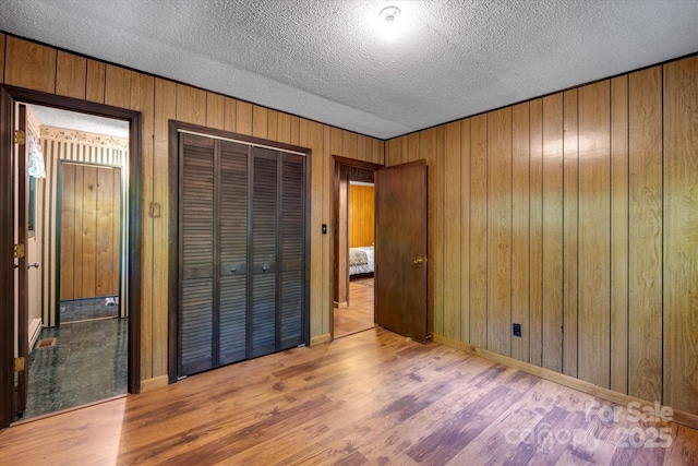 unfurnished bedroom with wood finished floors, a textured ceiling, a closet, wood walls, and baseboards