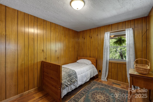 bedroom featuring wood finished floors, wood walls, baseboards, and a textured ceiling