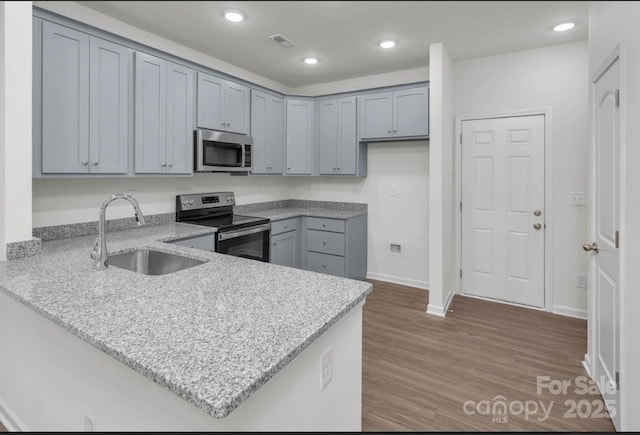 kitchen featuring appliances with stainless steel finishes, a sink, a peninsula, wood finished floors, and light stone counters