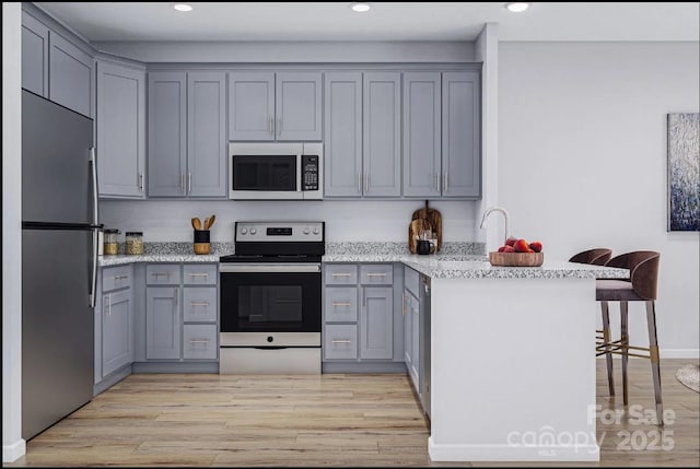 kitchen featuring appliances with stainless steel finishes, gray cabinetry, a peninsula, light wood-style floors, and recessed lighting