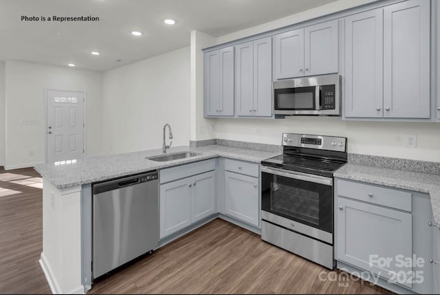 kitchen with stainless steel appliances, a sink, dark wood-type flooring, a peninsula, and recessed lighting