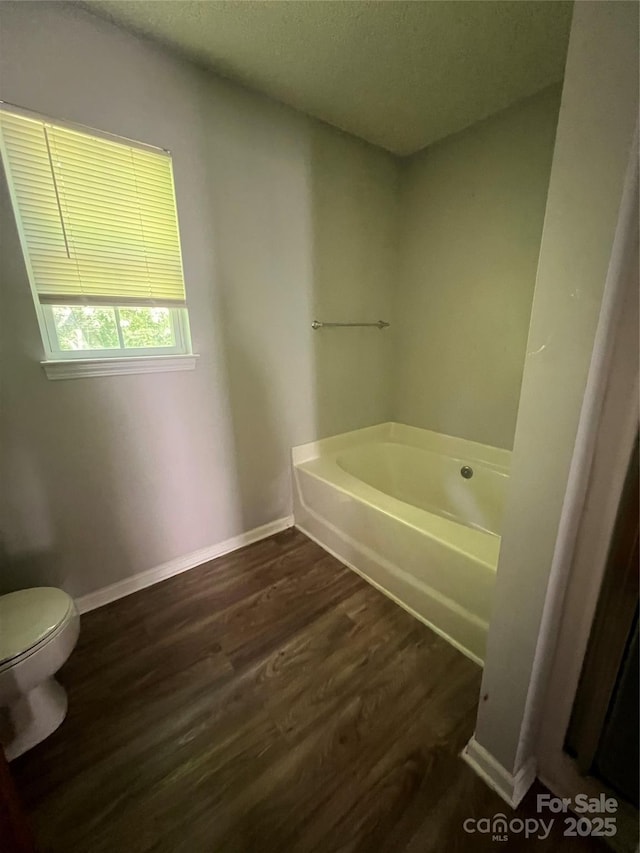 bathroom with wood finished floors, a garden tub, toilet, baseboards, and a textured ceiling