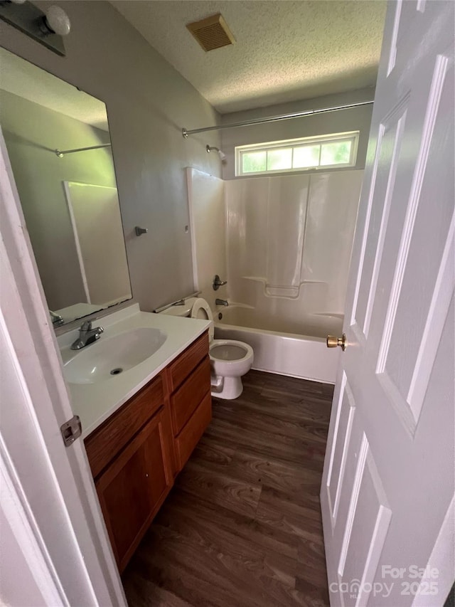 bathroom with wood finished floors, bathing tub / shower combination, vanity, a textured ceiling, and toilet