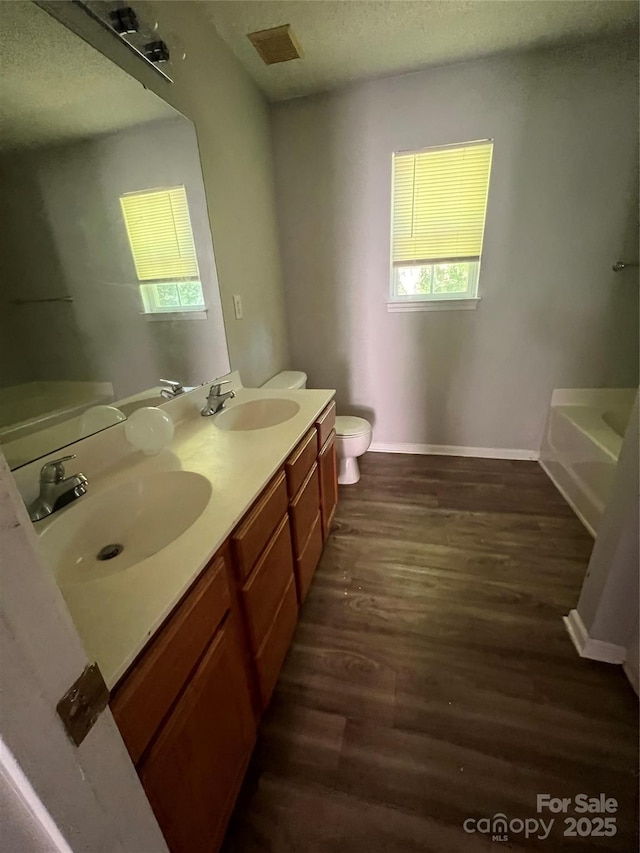 bathroom featuring wood finished floors, toilet, a tub, double vanity, and a textured ceiling