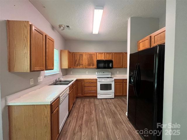 kitchen featuring black appliances, wood finished floors, a sink, a textured ceiling, and light countertops