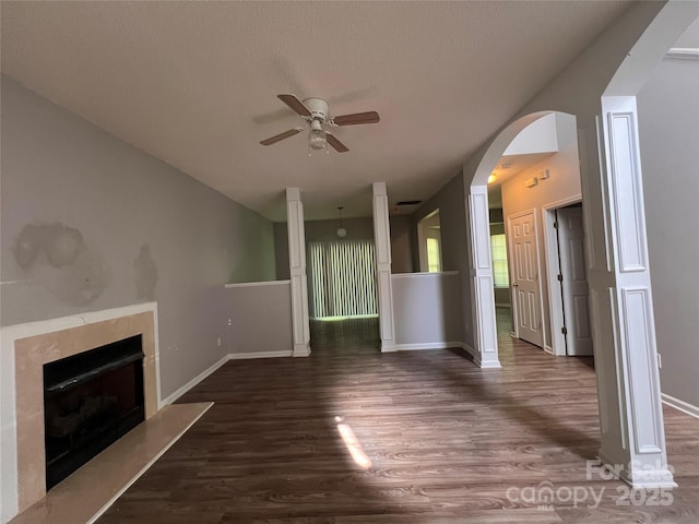 unfurnished living room featuring a ceiling fan, dark wood-style floors, arched walkways, a fireplace, and vaulted ceiling
