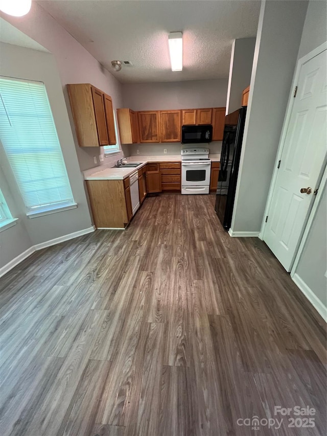kitchen featuring black appliances, dark wood-type flooring, light countertops, brown cabinetry, and baseboards