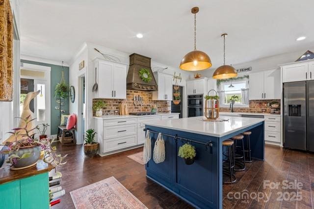 kitchen with stainless steel fridge with ice dispenser, premium range hood, tasteful backsplash, light countertops, and black stovetop