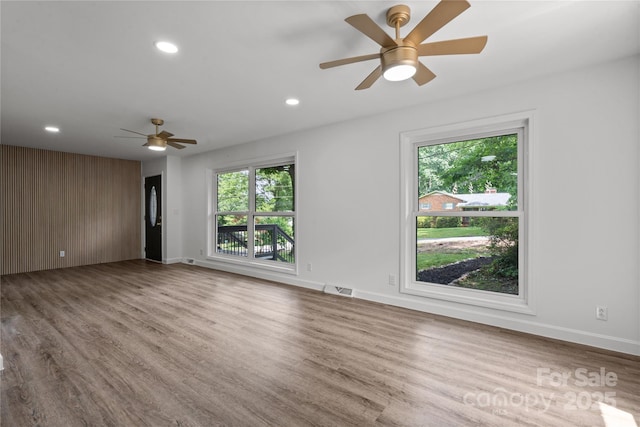 empty room with a ceiling fan, healthy amount of natural light, wood finished floors, recessed lighting, and baseboards