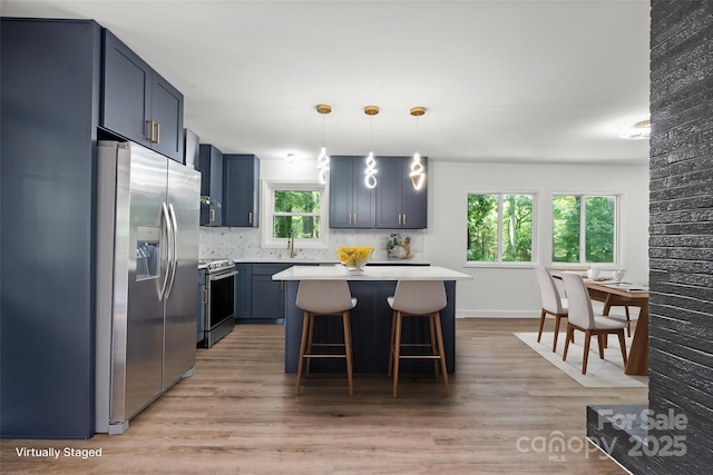 kitchen featuring appliances with stainless steel finishes, a sink, light countertops, a breakfast bar area, and light wood-style flooring