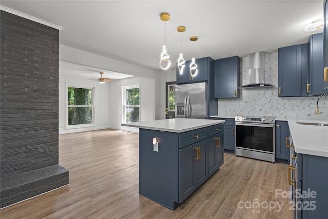 kitchen with wall chimney exhaust hood, stainless steel appliances, blue cabinets, light wood finished floors, and tasteful backsplash