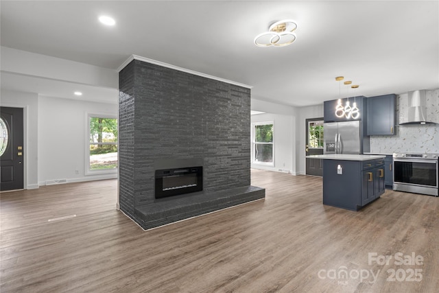 kitchen with appliances with stainless steel finishes, blue cabinetry, open floor plan, wall chimney exhaust hood, and healthy amount of natural light