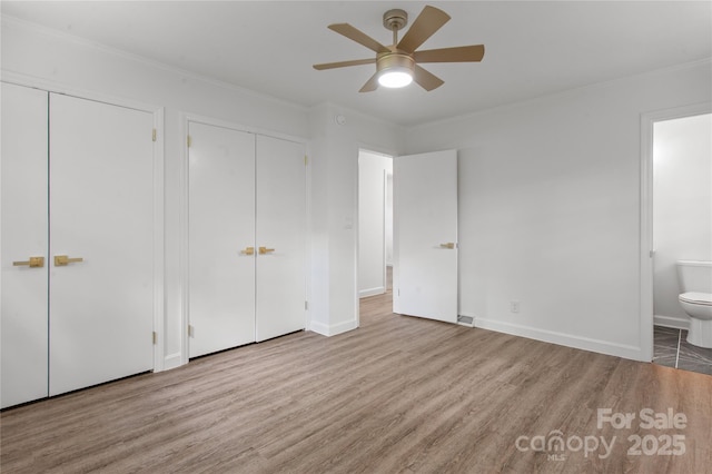 unfurnished bedroom featuring multiple closets, wood finished floors, crown molding, ensuite bathroom, and baseboards