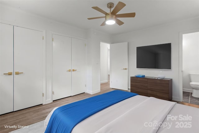 bedroom featuring wood finished floors, multiple closets, ornamental molding, ensuite bathroom, and ceiling fan