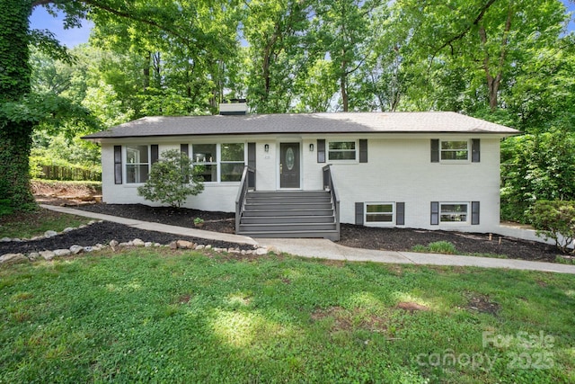 ranch-style house featuring a front yard, a chimney, brick siding, and view of wooded area