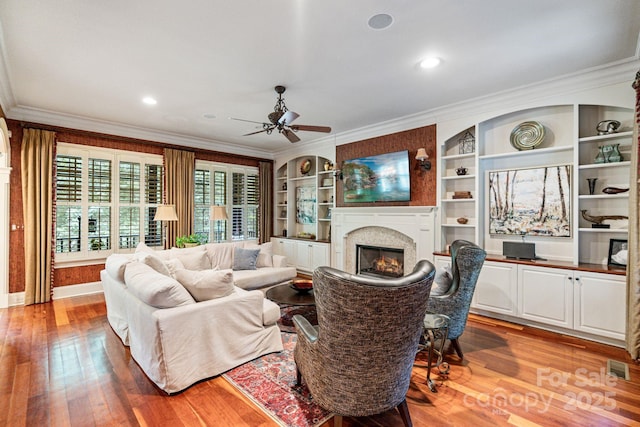8534 Highgrove St, Charlotte, NC 28277 - living room with a glass covered fireplace, light wood-style flooring, ornamental molding, a ceiling fan, and built in features