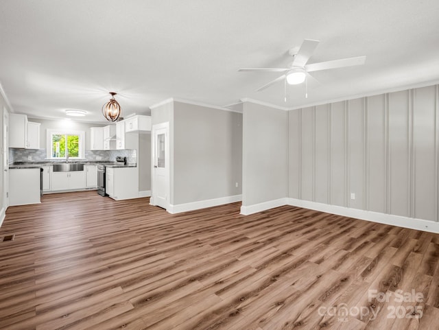 411 W Sycamore St, Lincolnton, NC 28092 - unfurnished living room featuring crown molding, light wood finished floors, a sink, a ceiling fan, and baseboards