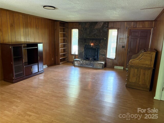 947 Ravendale Dr, Charlotte, NC 28216 - unfurnished living room with wood walls, a textured ceiling, healthy amount of natural light, and light wood-style flooring
