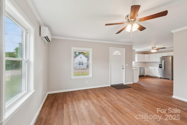unfurnished living room with a wall mounted air conditioner, ceiling fan, crown molding, light wood-type flooring, and baseboards
