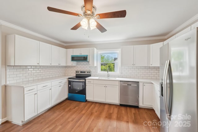 kitchen featuring stainless steel appliances, a sink, crown molding, tasteful backsplash, and light countertops