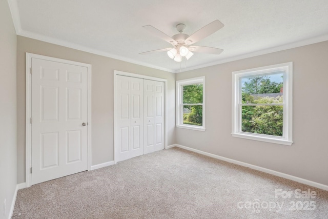 unfurnished bedroom with carpet, crown molding, baseboards, a closet, and ceiling fan