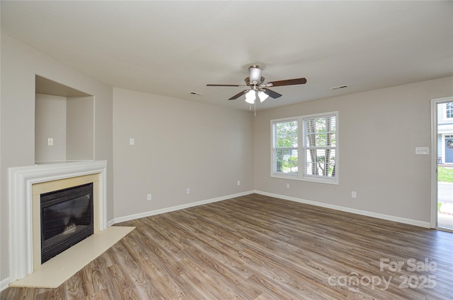 unfurnished living room featuring wood finished floors, a ceiling fan, baseboards, and a glass covered fireplace