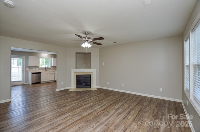 unfurnished living room featuring wood finished floors, a ceiling fan, baseboards, a glass covered fireplace, and a sink