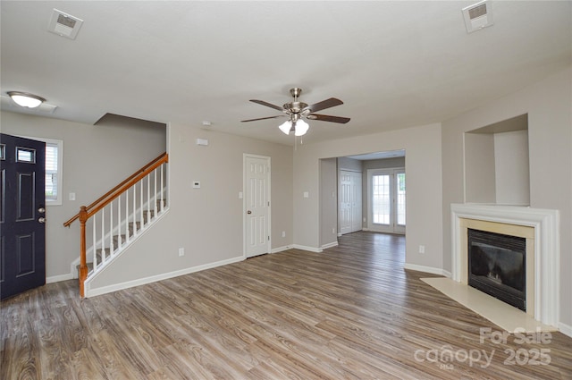 unfurnished living room with stairway, light wood-style floors, ceiling fan, and baseboards