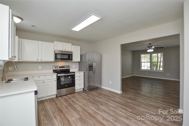 kitchen with appliances with stainless steel finishes, a sink, light wood-type flooring, light countertops, and white cabinetry