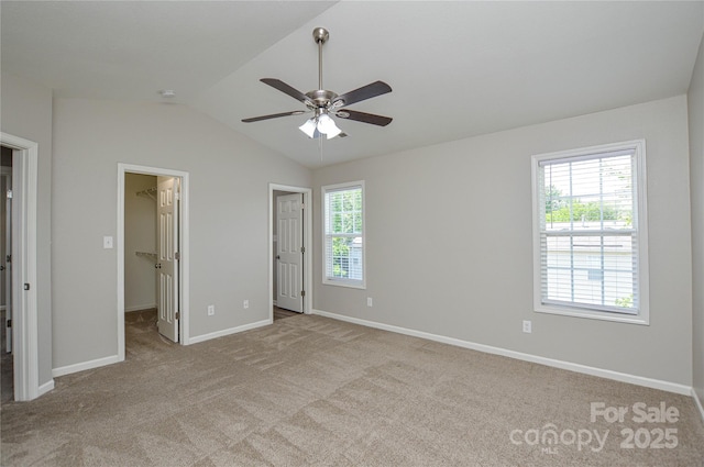 unfurnished bedroom with a walk in closet, carpet flooring, lofted ceiling, baseboards, and a ceiling fan