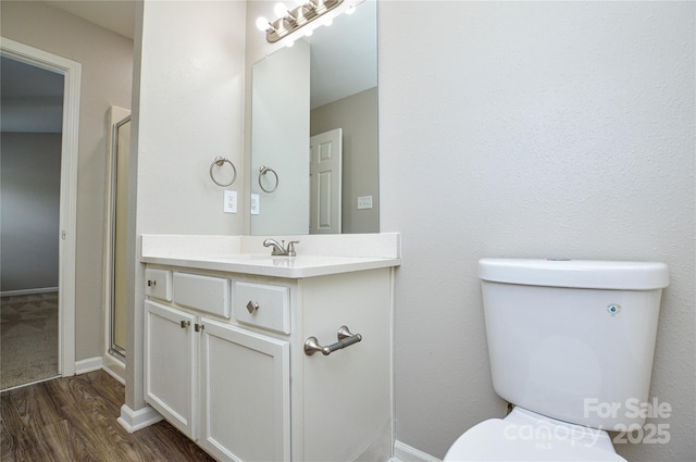 bathroom featuring toilet, wood finished floors, a stall shower, vanity, and baseboards