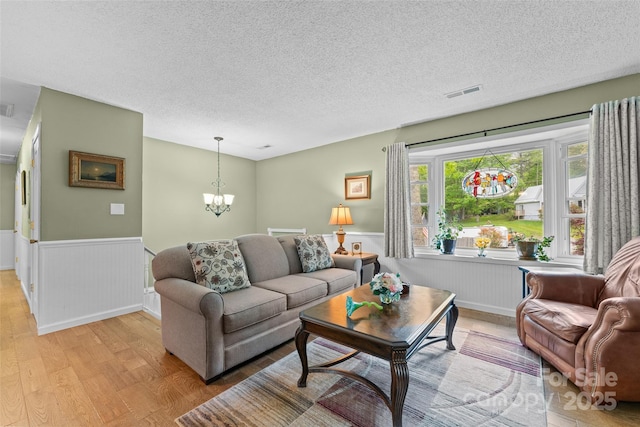 living room with light wood finished floors, wainscoting, a chandelier, and a textured ceiling