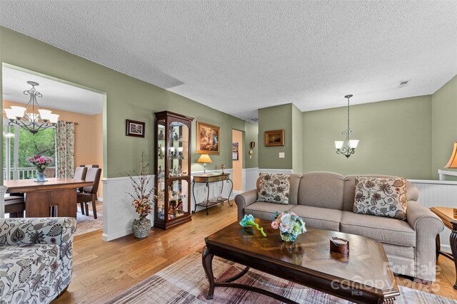 living area featuring a chandelier, a textured ceiling, light wood-type flooring, and a wainscoted wall
