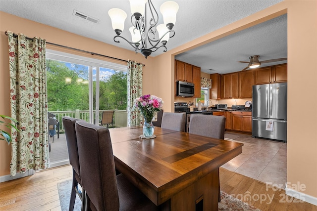 dining room featuring a chandelier, light wood-type flooring, a ceiling fan, and a textured ceiling