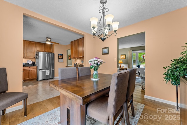 dining area with a chandelier, light wood finished floors, baseboards, and a textured ceiling
