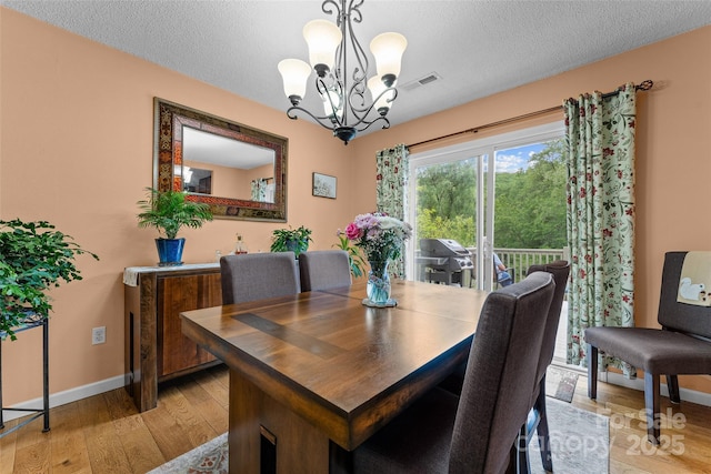 dining room featuring a chandelier, light wood finished floors, a textured ceiling, and baseboards