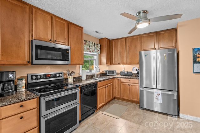 kitchen featuring stainless steel appliances, a sink, dark stone countertops, a textured ceiling, and ceiling fan