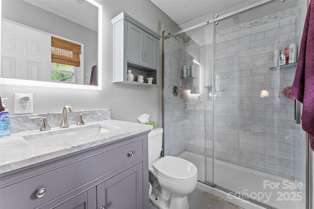 bathroom with a textured ceiling, toilet, a shower stall, and vanity