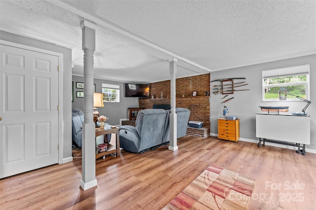 living room with a textured ceiling, brick wall, light wood-style floors, a fireplace, and baseboards