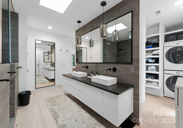 2913 Lake Ave, Charlotte, NC 28208 - full bathroom with stacked washer / dryer, wood finished floors, a skylight, double vanity, and tile walls