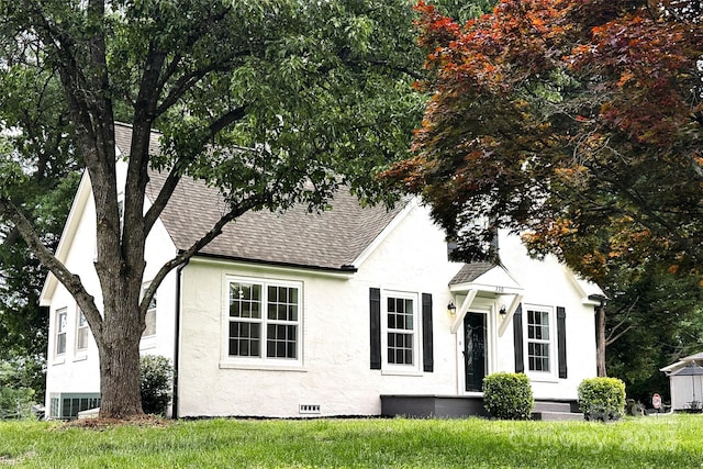 view of front facade with a shingled roof, stucco siding, and a front lawn