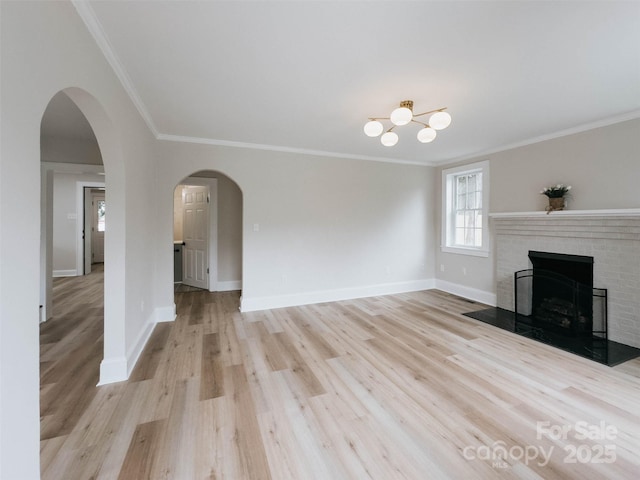 unfurnished living room with ornamental molding, a fireplace, light wood-style flooring, baseboards, and arched walkways