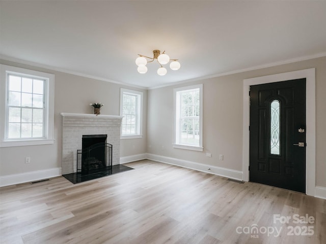 unfurnished living room featuring crown molding, light wood finished floors, baseboards, a brick fireplace, and a chandelier